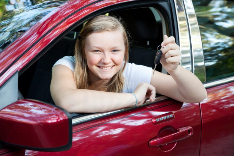 teenage girl sitting in her new car, holding the keys.