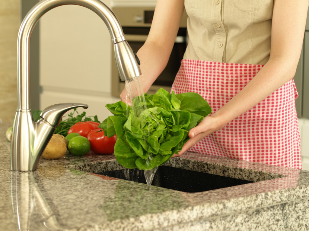 A woman washes lettuce for a salad under running tap water